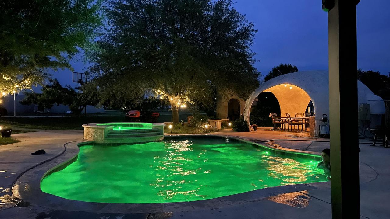 The pool is lit up with bright green lights at night with the kitchen-dining area in the background.